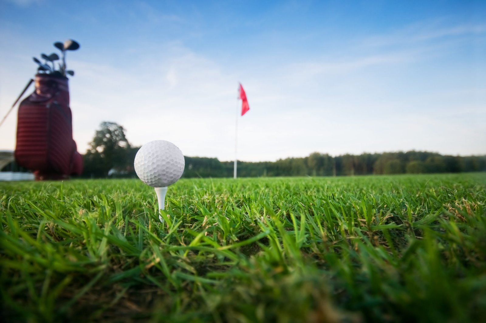 Balle de golf posée sur un tee, sac et drapeau en arrière-plan